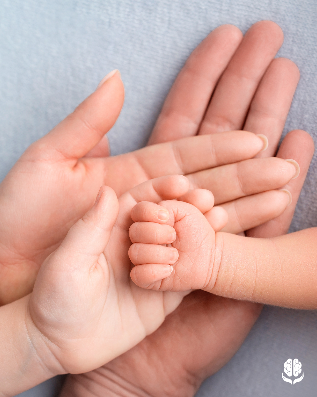 Handen van volwassenen die de hand van een baby vasthouden als symbool voor erfelijkheid, familielijnen en migraine die binnen families kan voorkomen.